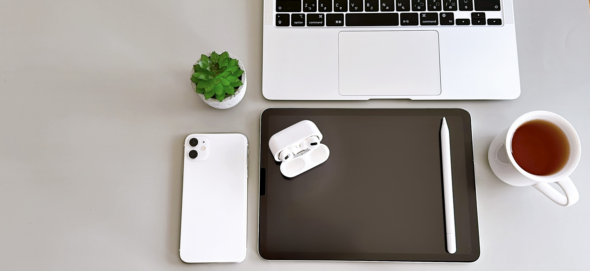 白いデスクの上にmacbookと黒いバインダー、さらにコーヒーカップがある。