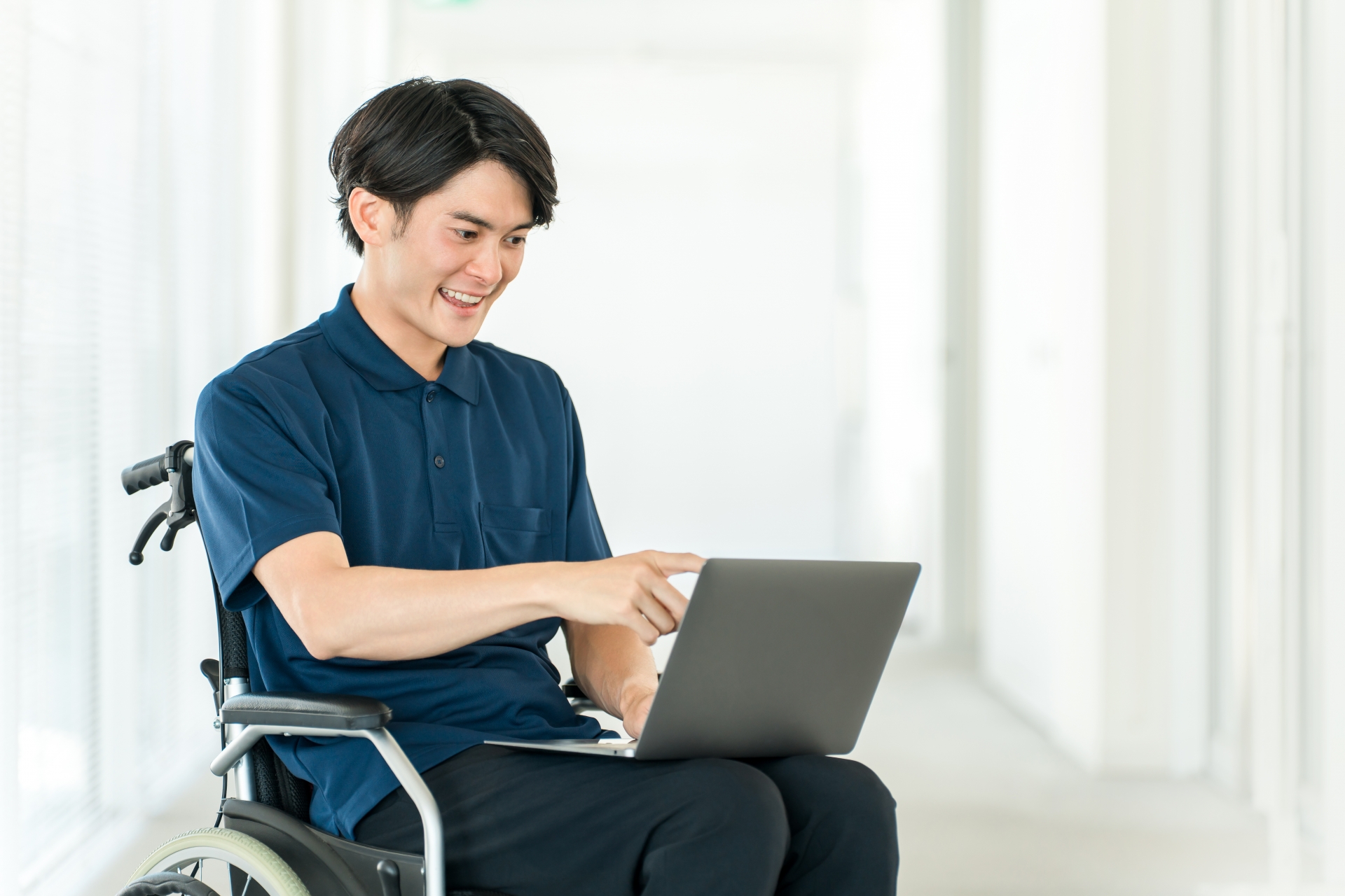 膝に置いたpcを指さしている車イスに座った男性