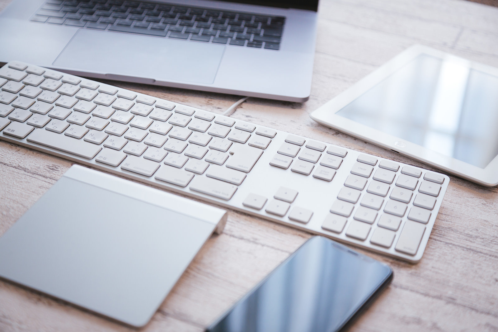 白いキーボード、macbook、ノートなどが机に置かれている