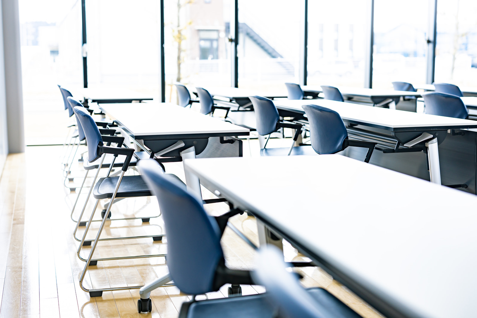 太陽光が差し込む白い机と青いパイプ椅子が均等に並べられた部屋