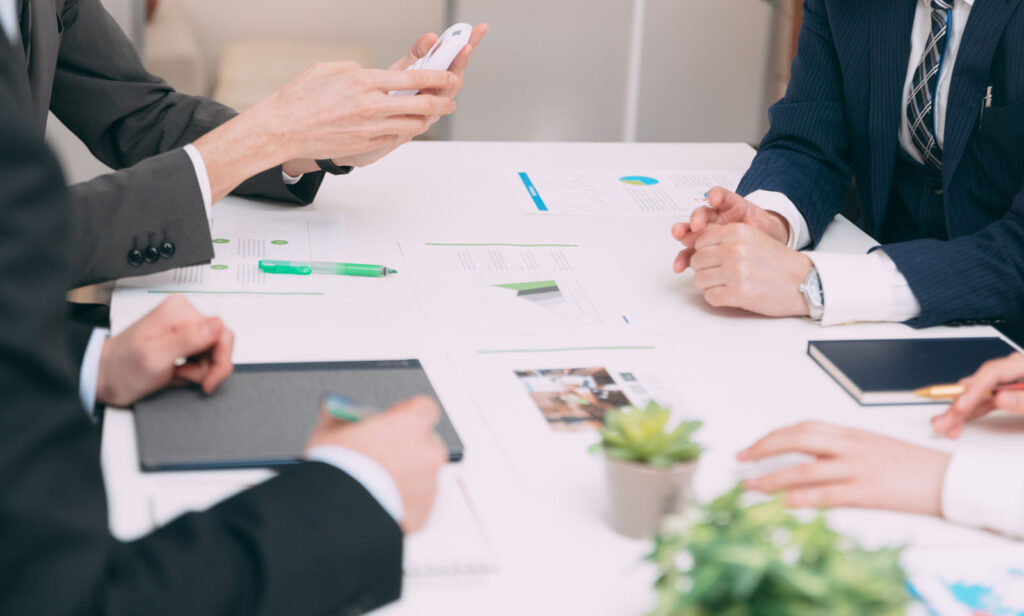 スーツを着た4人が2人ずつ向かい合って相談している。顔は映っていない。