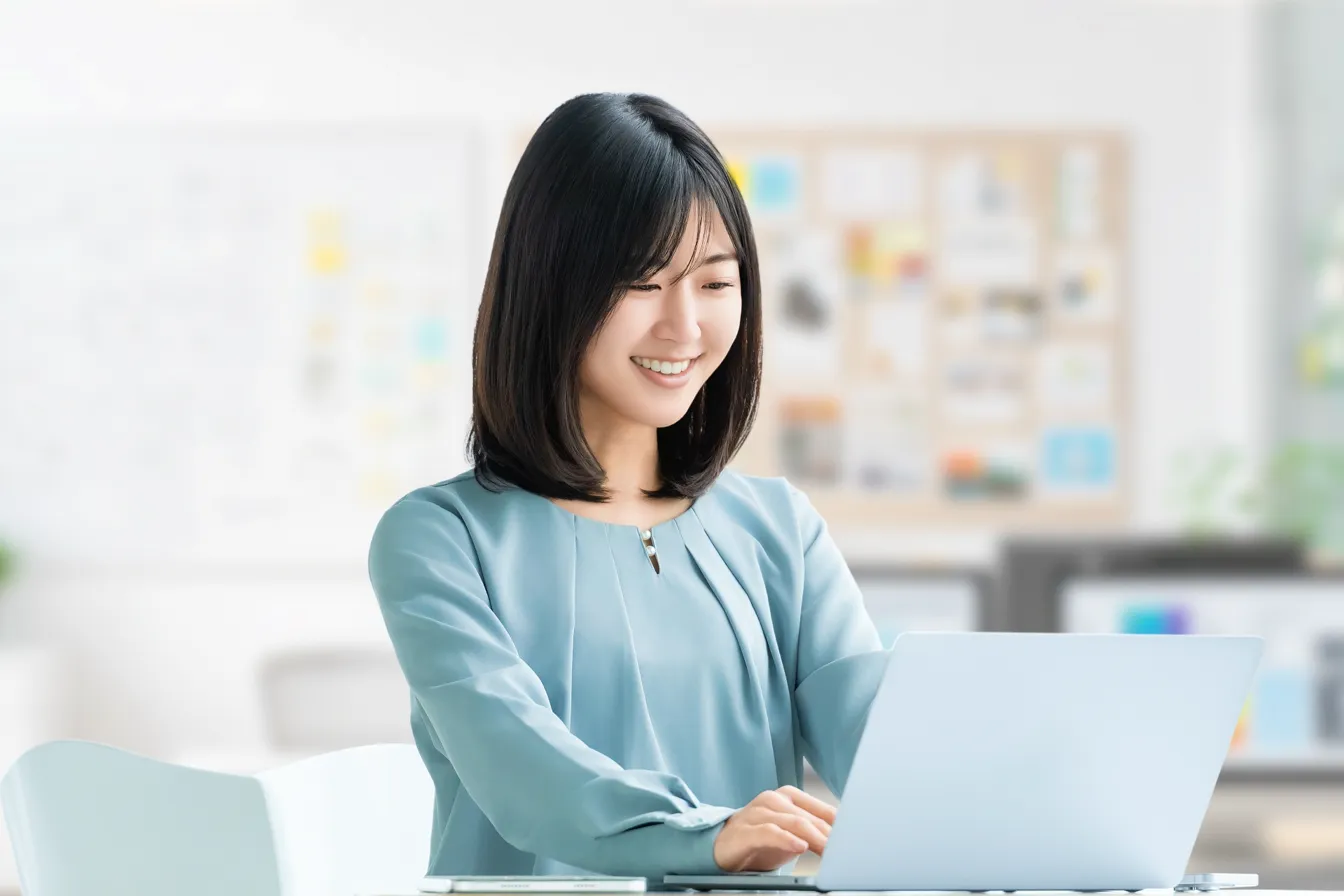 水色の服を着た女性が笑顔でPCを操作している