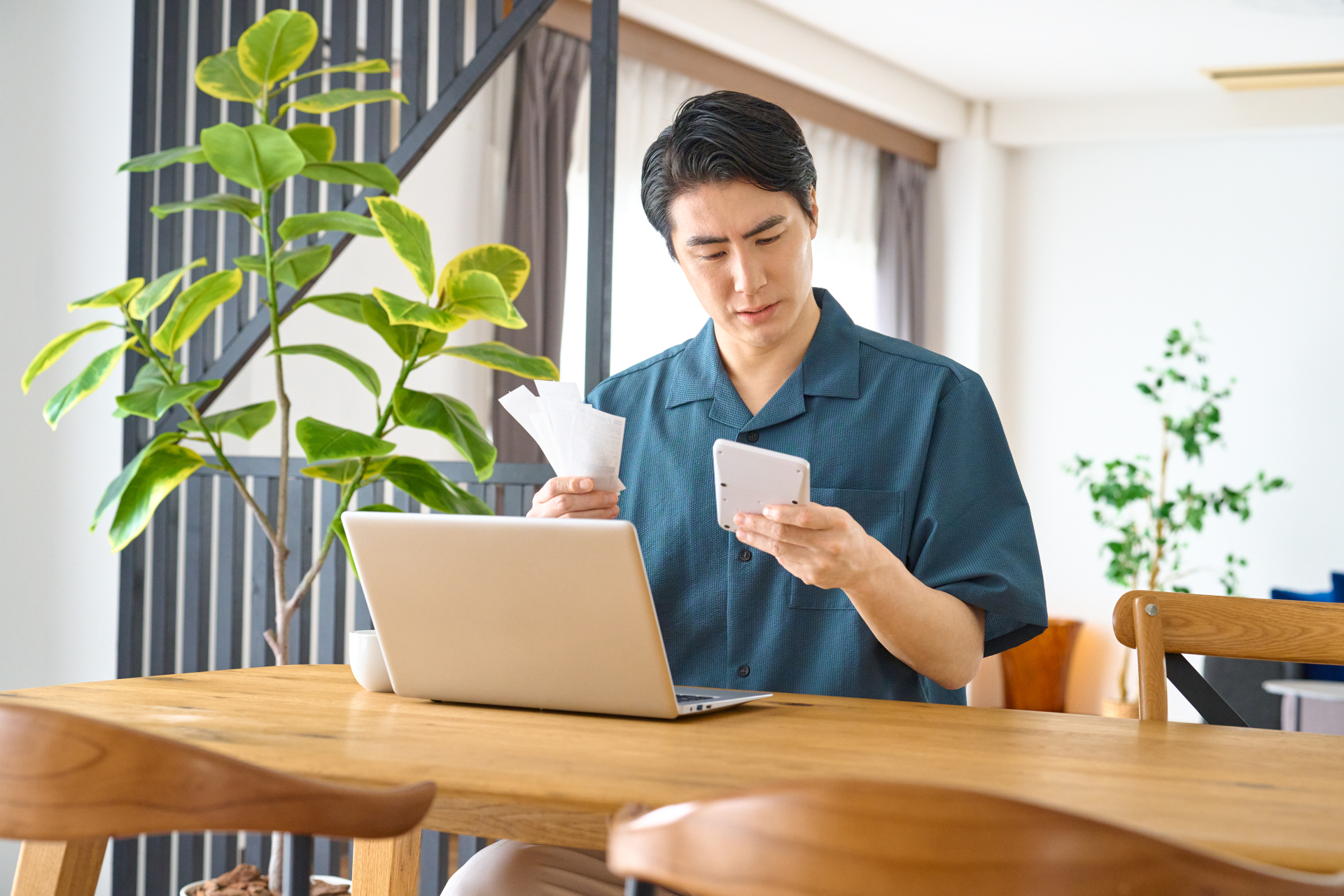 PCとデスクの前で左手に持っているメモを見ている男性