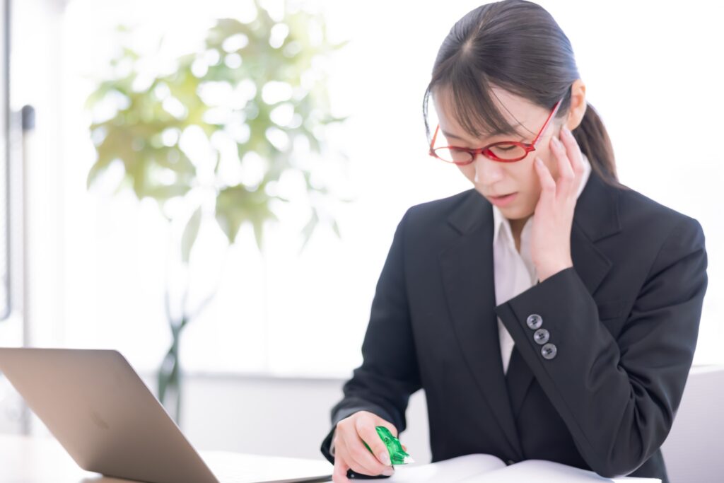 赤い眼鏡をかけたスーツを着た女性がうつむいている。